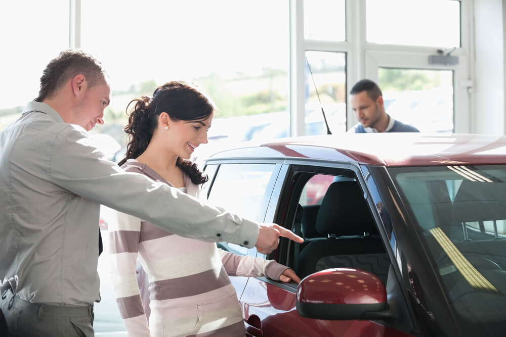Car dealer pointing the interior of a car with a woman in a car shop